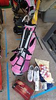 Overview of entire lot showing pink Callaway golf bag with several golf clubs, white golf sneakers, golf balls, tees, and golf ball box
