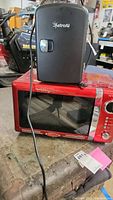 Wide shot showing the Nostalgia red microwave with glass door, chrome buttons, and the black AstroAI mini cooler placed on top.