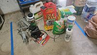 Overview of assorted pest control products including spray bottles, chemical bags, and a metal trap on a concrete floor.