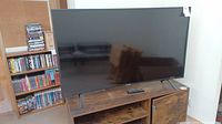Samsung TV on wooden stand with shelves and DVDs in background.