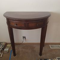 Front view of the wooden side table showing semi-circular shape and pull out drawer with two knobs.