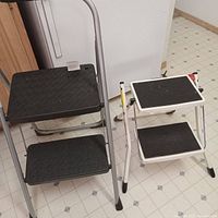 Photo showing both step ladders side by side with black, non-slip steps and metal frames.