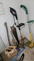 Photo showing two electric trimmers, a vintage hand saw, an axe, and a bag containing hand tools