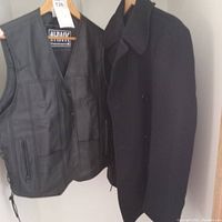 Front view of black leather vest and navy pea coat hanging side by side