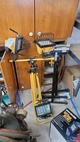 Two portable work lights mounted on adjustable stands along with roller stands and cardboard box nearby, wooden cabinet background