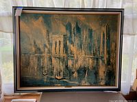 Full view of the framed painting showing cityscape over a river, with noticeable damage in the upper right corner.