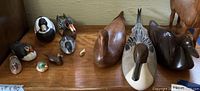 Photo of multiple artisan-carved duck decoys and smaller bird figures arranged on a wooden surface showing variety in size and finish.