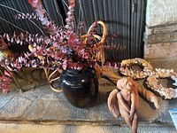 Cherub statue seated on stone hearth alongside black vase with faux eucalyptus flowers, shell wreaths, a basket, and rustic wood decoration.