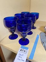 Six cobalt blue glass stemware glasses arranged on a shelf showing their round bowl shape and thick stems.