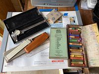 Drafting tools including pastel box, colored pencils, dial caliper case, slide rule case, and portable drawing board.