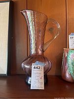 Side view of a purple translucent handblown glass jug with bulbous base and tall flared neck with handle, showing the full shape and color