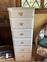 Front view of repainted white lingerie chest in a living room setting, showing six drawers with metal handles.