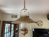 Front view of brass-toned Mid-Century Modern hanging light with scalloped bell-shaped shade and frosted glass globe