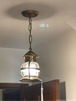 Vintage hanging light fixture with glass globe and metal frame hanging from ceiling chain mount, lit on showing illumination and metal casing details.