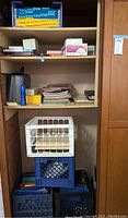 Photo of the shelving unit containing plastic milk crates, file folders, notebooks and some other office supplies.