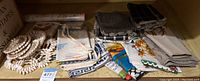 Photo showing shell trivets coiled and stacked on the left with folded table linens in napkins and towel style on the right in various colors and patterns.