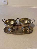 Photo showing the weighted creamer and sugar bowl placed on the oval serving plate, highlighting the set configuration and reflective surface.