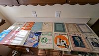 A long view of a set of 13 vintage sheet music sheets laid out, showing variety of cover colors and designs