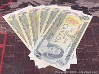 Front arranged view of six 1 dollar Canadian banknotes stacked fanned out.