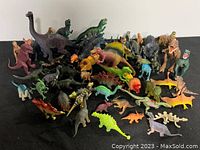 Assortment of over 35 colorful dinosaur plastic figurines of various species laid out on black surface.