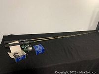 Two fishing rods with reels and additional reels in boxes on black cloth surface