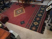 Full view of the red area rug under furniture showing overall pattern and fringe
