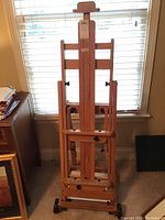 Front view of wooden adjustable artist's easel standing upright against a window with natural light.