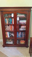 Front view of wooden bookcase with glass doors filled with books.