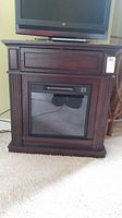 Front view of electric fireplace heater in dark wooden cabinet with glass front and control buttons.