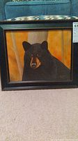 Full view of framed bear canvas art resting on carpet showing front with bear portrait.