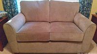 Front view of brown upholstered loveseat showing two seat cushions and two back cushions with padded arms.
