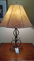 Full lamp with wrought iron base and tan lampshade, showing shape and overall look.