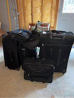 Six black luggage pieces grouped on a concrete floor showing sizes and shapes