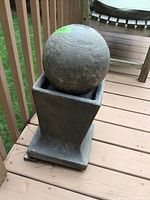 Front view of a cement outdoor fountain featuring a large spherical top on a square base.