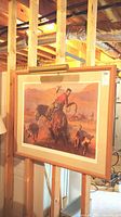 Photo of framed cowboy western wall art print showing signature and attached frame lamp mounted above the frame.