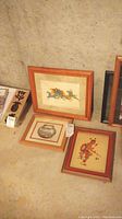 Three medium-sized framed wall art pieces resting on a concrete floor showing all three artworks and frames.