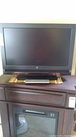 Photo showing the Westinghouse 26 inch TV with black frame, positioned on furniture with the remote lying in front.