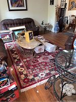 Area rug on hardwood floor under furniture including a glass coffee table and brown leather seating. Shows overall pattern and wear.