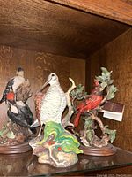 Three bird sculptures on shelf with detailed bases and naturalistic foliage