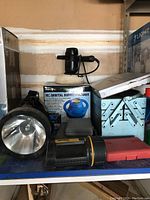 Orbital buffer/polisher box, buffered tool, metal toolbox, two flashlights, assorted hand tools and drill bits on a shelf.