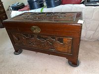 Front side view of the Asian-themed carved cedar chest showing the detailed carved panel and brass lock.