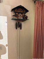Full view of the cuckoo clock mounted on wall with weights and chains hanging down.
