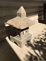 Full view of the concrete garden lantern on a porch floor, showing the pagoda-style roof and square base with arch cutouts.