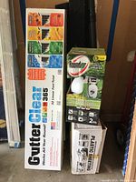 Boxed Gutter Clear gutter cleaning system, Roundup sprayer, and box of plastic sheeting arranged upright.