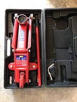 Image of red MVP hydraulic floor jack stored in black plastic carrying case, including handle and a socket wrench