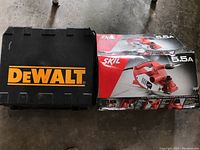Two boxed items on concrete floor: a DeWalt drill kit case and a SKIL planer kit box with 5.5A specification on the front.