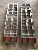 Two aluminum automobile ramps laid flat showing metal grid structure with red plastic end caps.