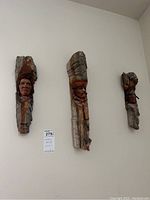 Three carved wood wall art pieces mounted on a wall, each showing a carved face with bark edges intact.