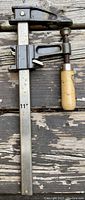 Photo of 11 inch F-clamp showing metal bar, adjustable sliding mechanism, screw clamp, and wooden handle on a weathered surface.