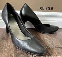 Pair of black women's heels size 9.5 on a wooden floor, showing shape and condition.